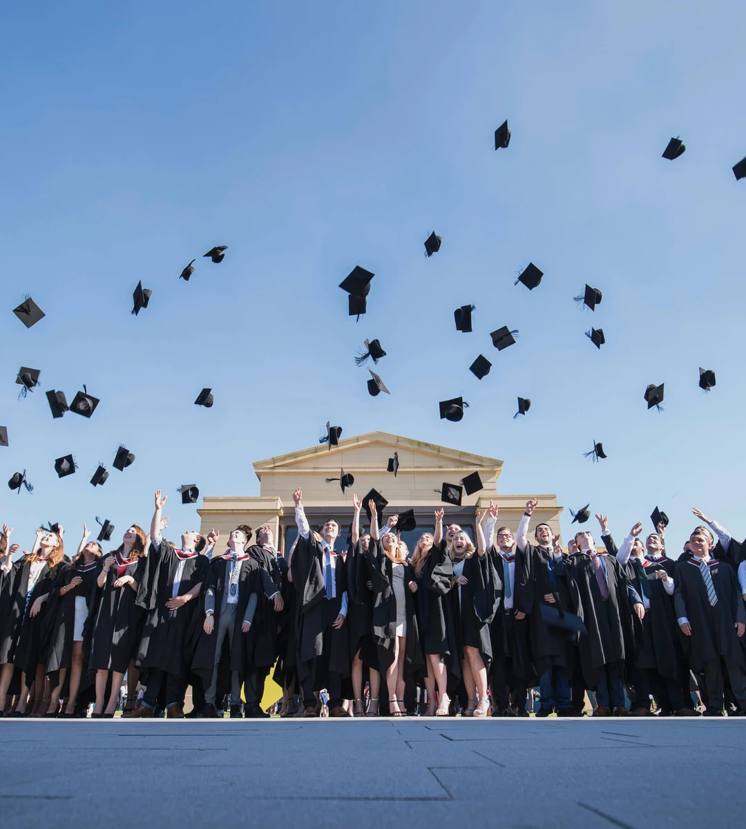 Выпускники Swansea University подбрасывают конфедератки перед корпусом кампуса